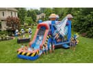 A large blue and red space-themed inflatable water slide and bounce house combo set up in a green backyard for a summer party. The inflatable features a giant space shuttle graphic and planets on the pillars. Children are sliding down into a splash pool w