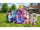 A magical unicorn-themed bounce house combo with a rainbow slide at a backyard birthday party in Houston. Three girls in rainbow tutus play in front of the inflatable, which features large unicorn graphics and a smiling star. This premium party rental is