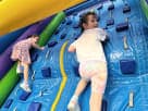 Two children climbing a 22ft blue rock wall rental in Austin with colorful handholds, ideal for all ages at San Marcos parties.